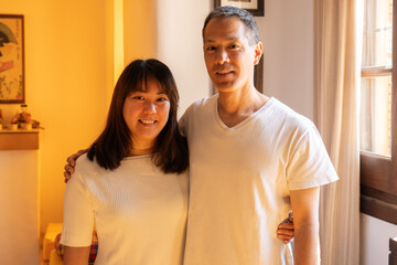 Adult siblings standing hugging each other of Japanese ethnicity, smiling and looking at the camera.
