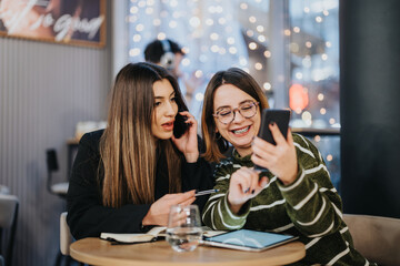 Two young females engaged in a collaborative work session at a cafe with smart phones and a digital tablet, conveying teamwork and connectivity.