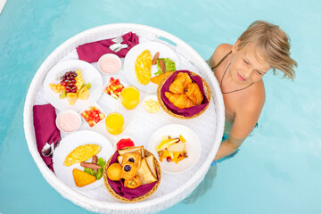 teenage boy with served floating tray in swimming pool with drinks and snacks on tropical island resort in Maldives, breakfast for romantic date or honeymoon in luxury hotel, travel concept