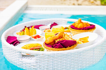 served floating tray in swimming pool with drinks and snacks on tropical island resort in Maldives, breakfast for romantic date or honeymoon in luxury hotel, travel concept