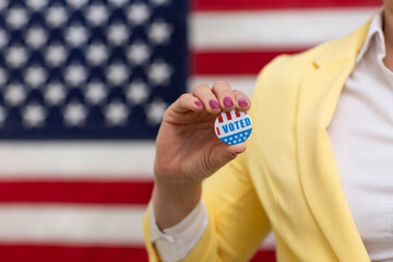 Voter woman holds in hand an USA badge on election day, USA flag background. Political election concept