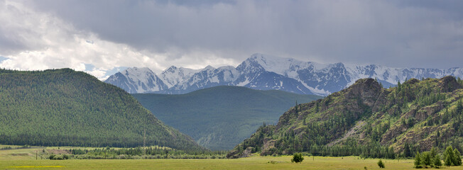 speaks in snow behind green mountains under gray clouds