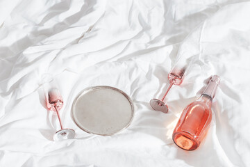 Pink champagne glasses with metal shiny and bottle of rose sparkling wine on white bed cloth....