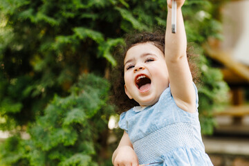 Very happy little joyful girl full of positive emotions in front of the green tree in the garden