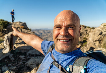 Hiker man takes a selfie pointing the peak of the mountain