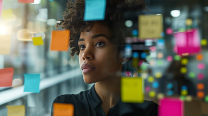 professional woman standing by a glass wall or window covered with colorful post-it notes