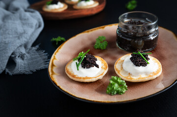 Black sturgeon caviar on mini pancakes blinis with sour cream and a glass jar.