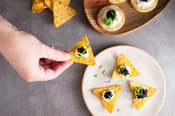Female hand holding nachos with sturgeon black caviar, seafood appetizer.