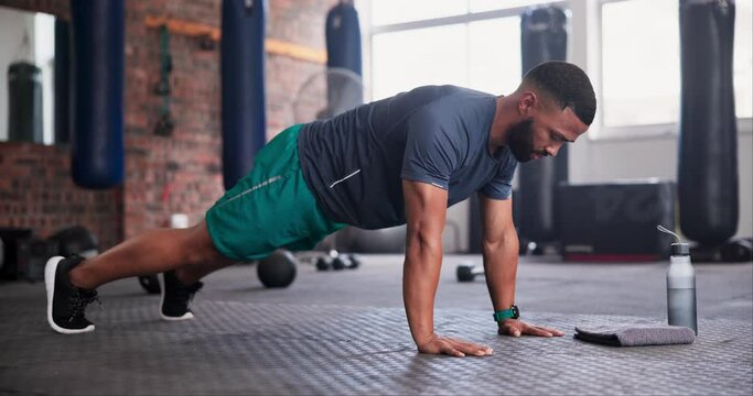 Black man, push ups and fitness for arm workout, exercise or training on floor at gym. Active African young male person lifting body in sports for muscle gain, strength or health and wellness at club