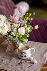 Obraz na płótnie Canvas a beautiful delicate spring white and pink bouquet of tulips, buttercups and muscari. floral arrangement with coffee mug, festive morning