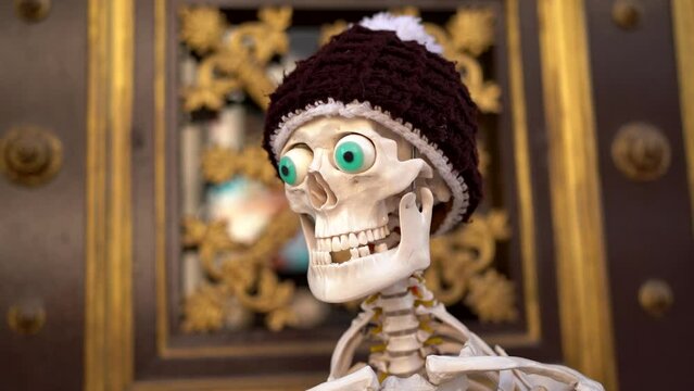 lose up of funny skeleton with green eyes and hat and missing teeth in front of golden door.