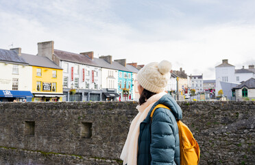 Unknown woman with backpack and winter hat enjoying a visit to a small town in Ireland with...