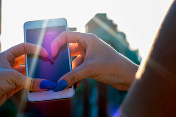 Close up view of woman in blue with blue nails making heart shape on smart phone on the roof of...