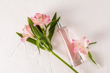 A chic bottle of women's perfume lies on a white background with delicate astromeria flowers. Top view. Empty bottle.
