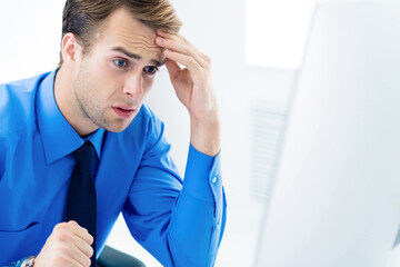 Portrait image - shocked or surprised unhappy businessman in confident blue shirt and glasses, with computer at office. Business, job and education concept.