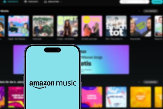 amazon music logo is displayed on an iPhone, website of the music streaming platform and online music store operated by Amazon behind, songs, subscribers