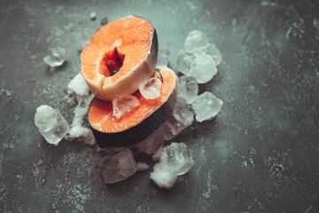 two pieces of salmon on ice cubes, close-up on a dark background in cold colors