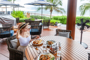 Casual dining by the sea, woman with hat savoring food at ocean view eatery.