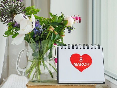 March 8. Bouquet of bright flowers standing in a vase and a postcard with a draw heart. Close-up, no people. Concept of preparation for a holiday. Congratulations for relatives, friends and colleagues