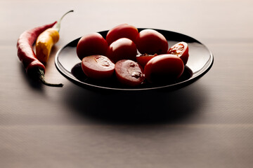 Cherry tomatoes, red and yellow peppers on a black round plate.