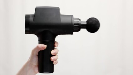 Close-up of woman's hand holding percussion massager with soft ball nozzle and turning on it gray background. Therapy for joint pain relief and physiotherapy