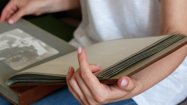 Person views photos in old family album, selective focus. Hand turns the pages of the huge photo album