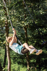A strong and healthy boy is having fun on a rope swing, the child is spinning fast and high, he is trying with all his might to keep himself from falling