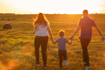Fototapeta na wymiar A blurred silhouette of a family of three on a meadow lit by the golden evening sun. Photographed from behind