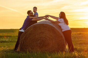A happy, cheerful family hugs and holds hands in the golden evening light by a large bale of straw