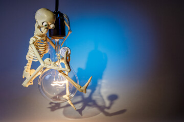 A funny and clever skeleton swinging on a light bulb, against a blue background, campaigns to save electricity. Free space for text