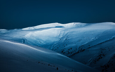 Snow-covered mountains illuminated by moonlight at blue hour.