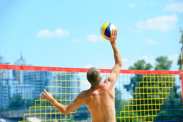 Beach volleyball. Young man volley player hitting over the net attacking