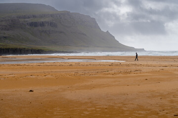 Fototapeta na wymiar Rauðasandur (Red Sand) beach in Westfjords, Iceland. One person in distance walking on beautiful endless beach with sand that changes color depending on the weather and time of day