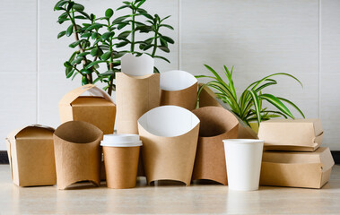 An assortment of eco-friendly disposable tableware on a light background with green plants. The concept of paper production to protect nature from plastic waste.