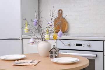 Home spring easter design in kitchen. Ceramic vase with spring branches with easter eggs, plates for two person in white kitchen. High quality photo.