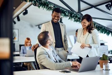 Three colleagues talking to each other, standing at the office, holding some documents.