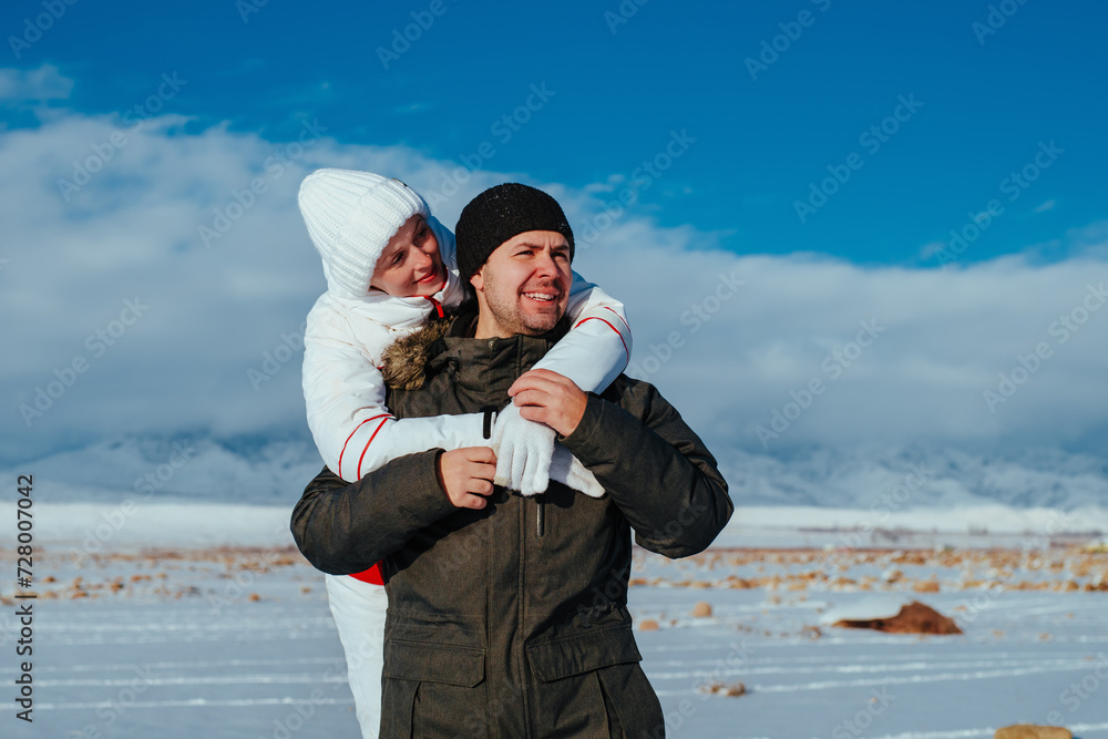 Sticker Young woman in winter costume embracing man on mountains background