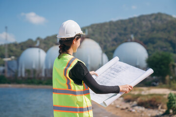 Confident female engineer in safety helmet and high-visibility vest holds blueprints with...