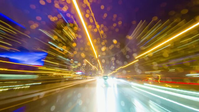 Back car window view of long exposure time laps of the highway in the city. City at night timelapse. Driving a car, the city at night. Camera at the vehicle back trunk glass. Rainy night soft glowing.