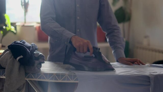 Latino man irons his children's clothes in the dining room. break with the concepts of gender and domestic tasks, equality and helping a man at home to his family and wife