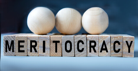MERITOCRACY - word on wooden cubes on a blue background with wooden round balls