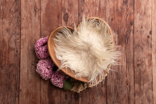 Basket for a photo shoot. Background for a newborn photo shoot. Basket with white fur. Basket with pink flowers. Bowl on a wooden floor.