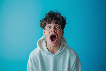 Fotobehang Young guy on a blue background screaming, frightened facial expression, panic scream © Olga