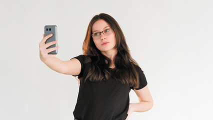 Mobile selfie. Digital lifestyle. Modern technology. Influencer girl in glasses taking photo on phone camera isolated on white empty space background.