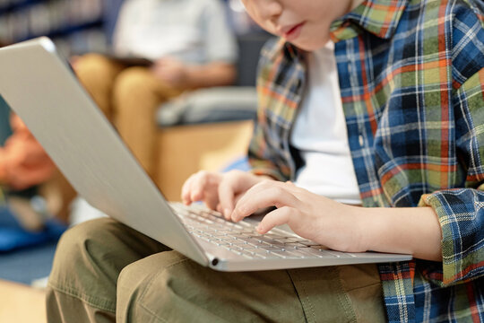 Close up of little boy using laptop in school library focus on hands typing with copy space
