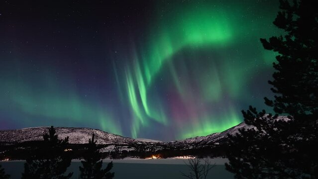 Aurora dancing vividly above a snow covered lake and a mountainous landscape in Bod&oslash;.
