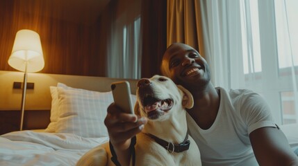Naklejka na ściany i meble Smiling african americane young man with lovely dog taking selfie in a hotel room. Pet friendly hotel, friendship, relax, social media profile picture and memory, influencer, pet owner 