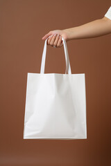 Woman's hand holding a white canvas shopping bag on brown background.