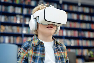 Minimal portrait of blonde young boy wearing VR headset in library with bookshelves in backgroundwith copy space