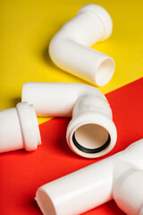 White sewage fittings lying on a colorful bright yellow-red background